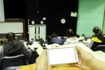 女使用白色移动电话与空白屏幕的教室和模糊背景学生在的研究测试测试考试从老师大讲座房间大学教室