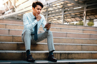 年轻的奋斗亚洲商人使用移动电话的城市坐着楼梯阅读认真主题通过智能手机