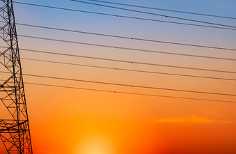 轮廓高电压电桥塔和电线与橙色天空电波兰人日落权力和能源概念高电压网格塔与线电缆分布站