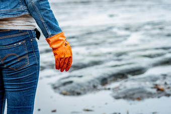 志愿者穿牛仔裤和长有袖的衬衫和穿橙色橡胶手套收集垃圾的海滩海滩环境女人清洁的海滩整理垃圾海滩