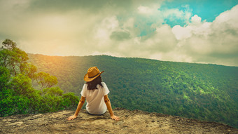 年轻的旅行女人穿他和坐着的前的山悬崖与放松情绪和看美丽的视图森林和蓝色的天空和云假期亚洲女人旅行独自一人