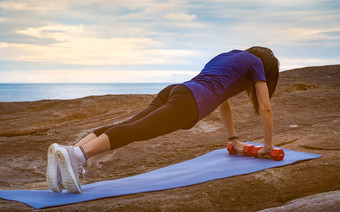 亚洲女人锻炼的早....石头海滩适合女人手持有红色的哑铃和<strong>推</strong>蓝色的瑜伽席为身体强度重量<strong>培训</strong>锻炼为健康的生活方式平屁股女人