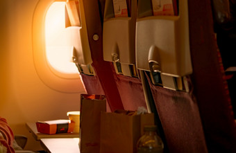 食物棕色（的）纸袋把塑料飞机托盘表格座位回来与模糊乘客手打开黑色的皮革袋阳光通过通过的经济类飞机窗口成的飞机