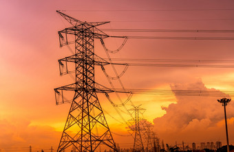 高电压电塔和传输行与橙色日落天空和城市景观现代办公室建筑背景电塔权力和能源为城市高电压网格塔