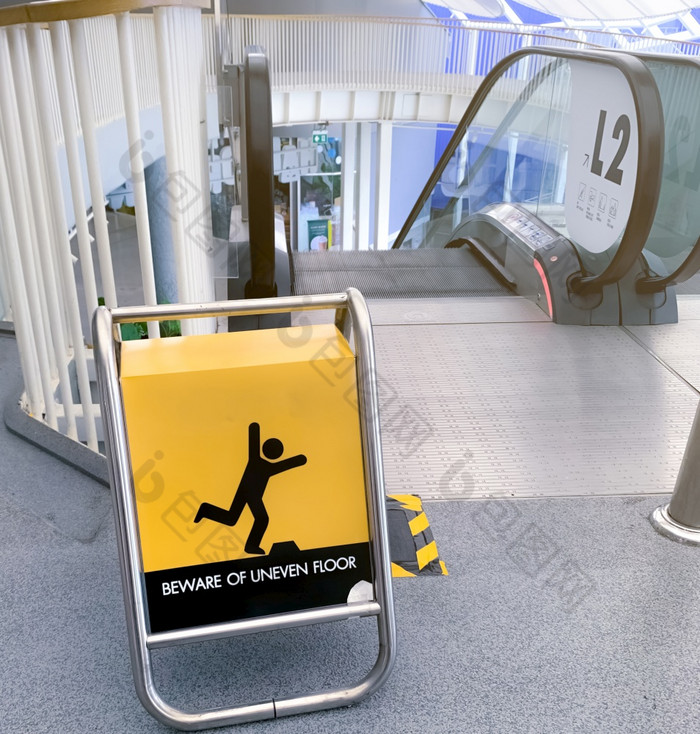 当心不均匀地板上警告标志黄色的董事会前面自动扶梯购物购物中心当心不均匀地板上警告标志为安全人行道之前黎明道路自动扶梯请注意为安全