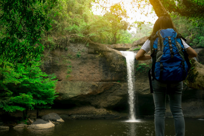 回来视图亚洲女人与背包看小瀑布的丛林活跃的女人与冒险旅行绿色森林徒步旅行徒步旅行女孩户外活动瀑布山