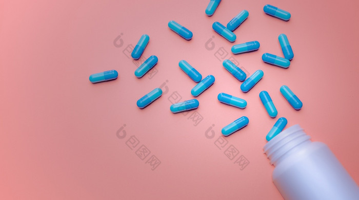 蓝色的胶囊药片传播出白色塑料药物瓶粉红色的背景药店横幅在线药店止痛药医学和抗生素药物电阻概念制药行业