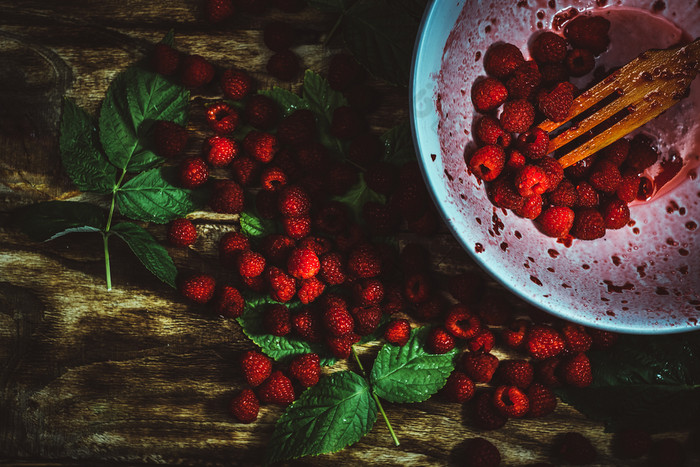 红色的新鲜的树莓棕色（的）乡村木背景碗与自然成熟的有机浆果与总花梗绿色叶子和木叉前视图平躺与复制空间碗与自然成熟的有机浆果与总花梗绿色叶子和木叉前视图