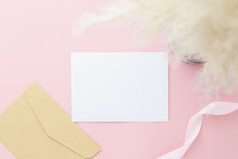 空白问候卡邀请模型信封与满天星花和丝带粉红色的柔和的纸背景平躺模型