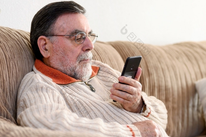 上了年纪的男人。使用手机坐着沙发首页在冠状病毒检疫上了年纪的男人。使用手机坐着沙发首页在冠状病毒检疫