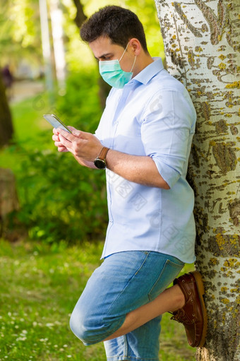 肖像英俊的男人。与医疗面具他的脸会说话的的电话和<strong>微</strong>笑快乐在户外后检疫由于新冠病毒病毒<strong>微</strong>笑快乐肖像英俊的男人。与移动电话和医疗面具他的脸发短信和<strong>微</strong>笑快乐在户外后检疫由于新冠病毒病毒