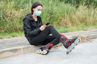 女人保护脸面具辊滑冰暂停坐着的街和使用移动电话在冠状病毒流感大流行爆发城市女孩使用电话穿辊溜冰鞋女人保护脸面具辊滑冰暂停坐着的街和使用移动电话在冠状病毒流感大流行爆发城市女孩使用电话穿辊溜冰鞋