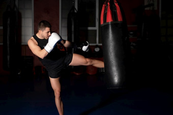 肌肉发达的英俊的跆拳道战斗机给有力的踢在练习轮与拳击袋高质量照片肌肉发达的英俊的跆拳道战斗机给有力的踢在练习轮与拳击袋