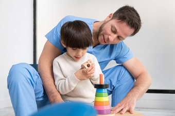 年轻的治疗师帮助可爱的小男孩谁有脑麻痹玩与发展中玩具康复诊所高质量照片年轻的治疗师帮助可爱的小男孩谁有脑麻痹玩与发展中玩具康复诊所