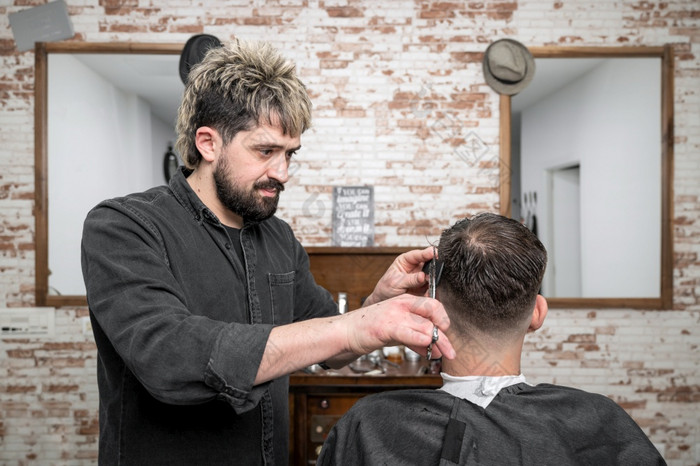 理发师切割头发与剪刀英俊的年轻的男人。高质量摄影理发师切割头发与剪刀英俊的年轻的男人。