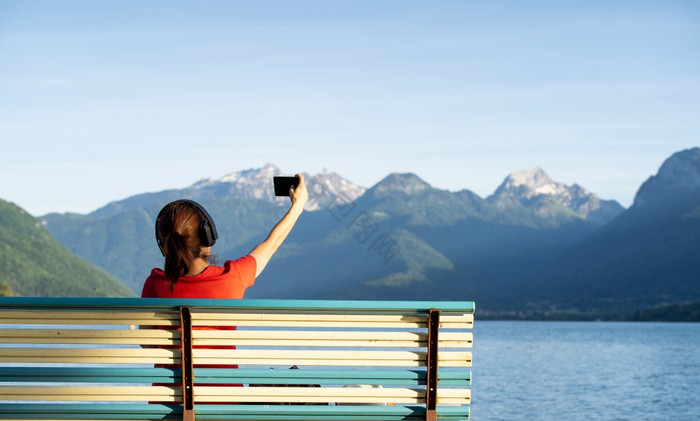 女孩与耳机采取自拍坐着板凳上前面的山湖生图片
