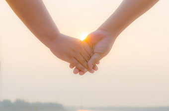 浪漫的夫妇与紧握手背光明亮的晚上太阳特写镜头概念上的图像爱