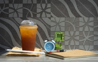 新鲜的冰茶外卖玻璃与稻草笔记本笔蓝色的报警时钟和小木图片框架的表格与瓷砖墙装饰背景让人耳目一新休闲活动概念