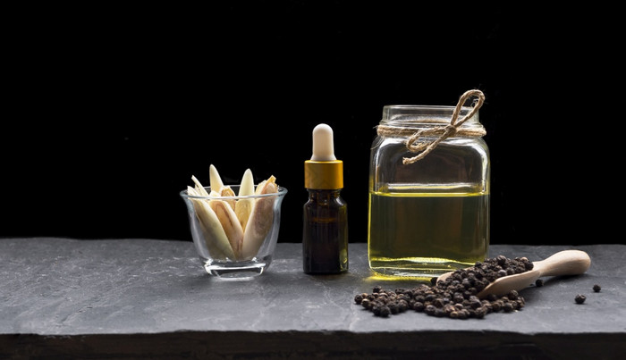 下降瓶与Herbal至关重要的石油玻璃Jar和柠檬草片小玻璃与黑色的花椒木勺子黑色的板岩板黑暗背景