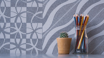 色彩斑斓的木铅笔玻璃Jar与小绿色仙人掌粘土能灰色桌面与摘要自然模式灰色的瓷砖墙背景