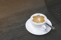 热卡布奇诺咖啡拿铁艺术白色陶瓷杯与部分移动PC电脑黑色的木表格咖啡馆