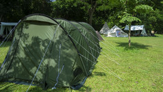 阳光和影子圆柱绿色帐篷与各种各样的帐篷绿色草坪上野营区域自然公园