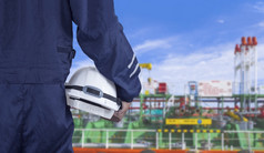 关闭工程师手蓝色的机械师连身裤持有白色安全头盔与模糊原油石油油轮蓝色的天空背景