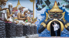 亚洲女旅游保护面具使用智能手机搜索信息而走看佛教艺术雕像周围泰国寺庙区域