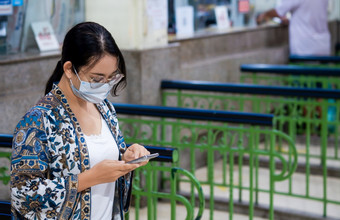 年轻的亚洲女游客休闲风格与保护面具使用智能手机票办公室区域火车站