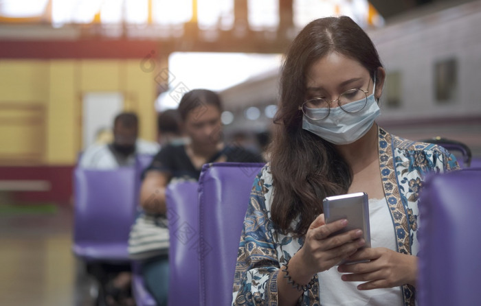 亚洲女乘客保护面具使用智能手机休息区域而等待为火车平台火车站