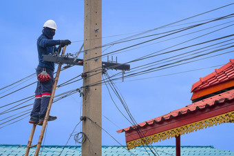 亚洲技术员木梯安装电缆行连接电话和互联网信号系统电波兰对蓝色的天空背景