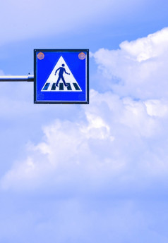开销电行人穿越标志与模糊白色云和蓝色的天空背景垂直框架