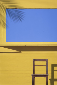 阳光和影子表面木椅子前面黄色的和蓝色的咖啡街亭垂直框架