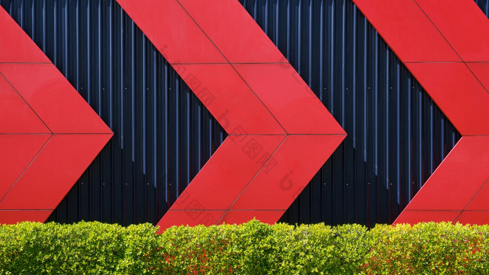 前面视图红色的箭头模式黑色的波纹金属墙后面绿色布什栅栏外体系结构装饰设计概念