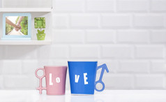 焦点夫妇蓝色的和粉红色的咖啡杯子白色表格与模糊装饰架子上瓷砖墙背景