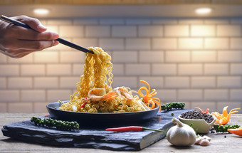 男人。手使用筷子挑选搅拌弗莱即时面条辣的海鲜黑色的陶瓷板的厨房