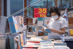 亚洲女人穿保护脸面具选择书书店购物购物中心区域