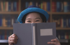 肖像亚洲女人微笑和看相机而隐藏她的脸后面书模糊书架上背景生活房间