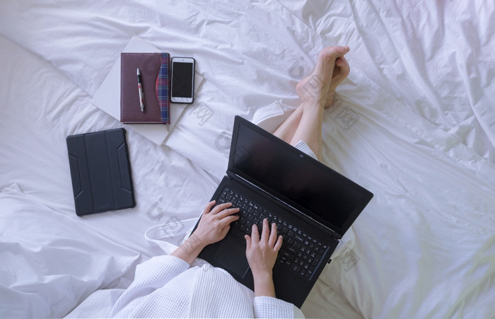 前视图女人白色浴袍使用移动PC电脑与书和各种各样的设备白色床上