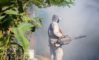 户外医疗保健工人使用成雾机喷涂化学消除蚊子和防止登革热发热的中间许多化学烟雾杂草丛生的贫民窟区域