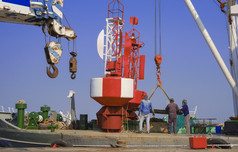 亚洲工人集团与起重机卡车是工作转移红色的球道浮标与钢板成的船港为安装交通标志的海