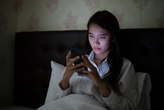 亚洲女人使用移动电话晚上的床上她微笑和享受首页