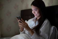 亚洲女人使用移动电话晚上的床上她微笑和享受首页