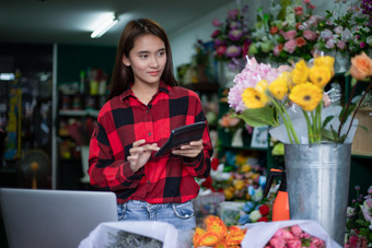 亚洲女人花店小业务花商店老板和她使用她的计算器和移动PC取订单为她的商店