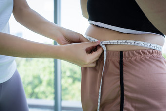 年轻的女教练测量脂肪层超重女人与腰围健身