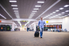 亚洲男人。旅行者与手提箱走和运输机场