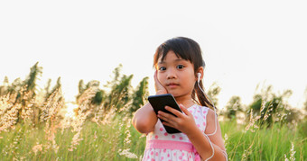 亚洲孩子女孩听音乐和唱歌从移动电话和快乐草地夏天自然
