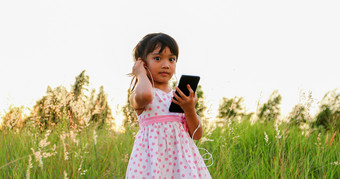 亚洲孩子女孩听音乐和唱歌从移动电话和快乐草地夏天自然
