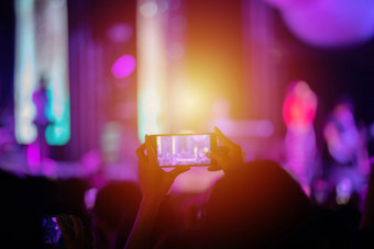 轮廓音乐会人群后视图节日人群提高他们的手和使用智能手机取照片和视频明亮的阶段灯