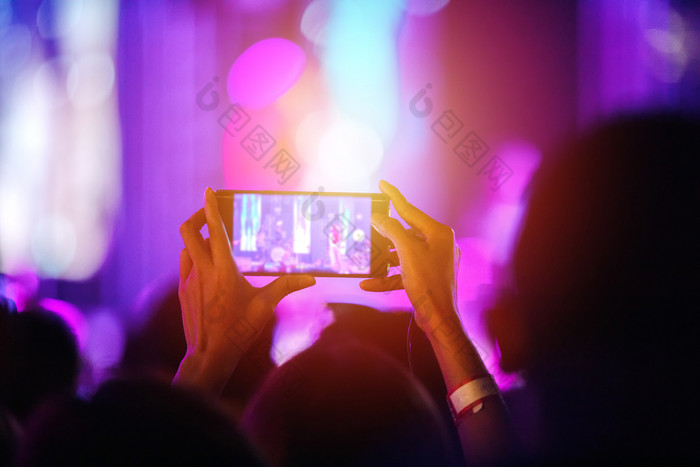 轮廓音乐会人群后视图节日人群提高他们的手和使用智能手机取照片和视频明亮的阶段灯